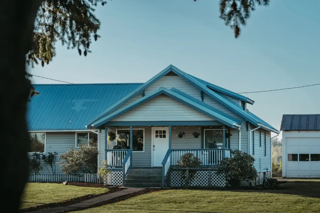 Blue-roofed farmhouse at 8668 Stayton Rd NE framed by trees on a sunny morning