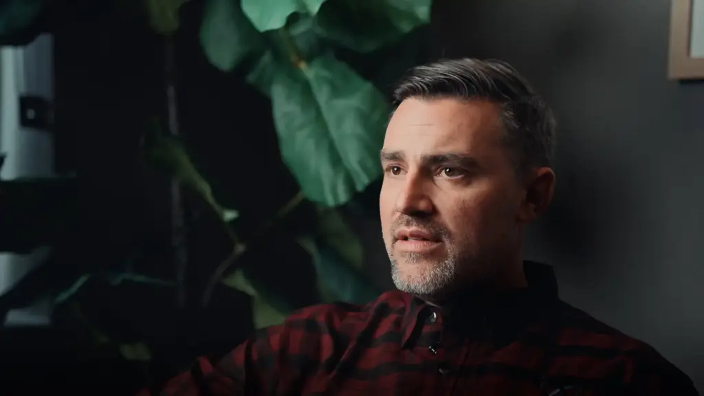 Man in a plaid shirt speaking during a documentary interview