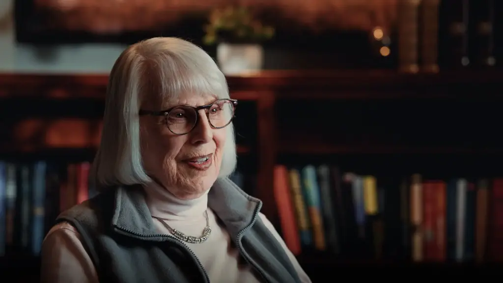 Smiling older woman with glasses interviewed in front of a bookshelf